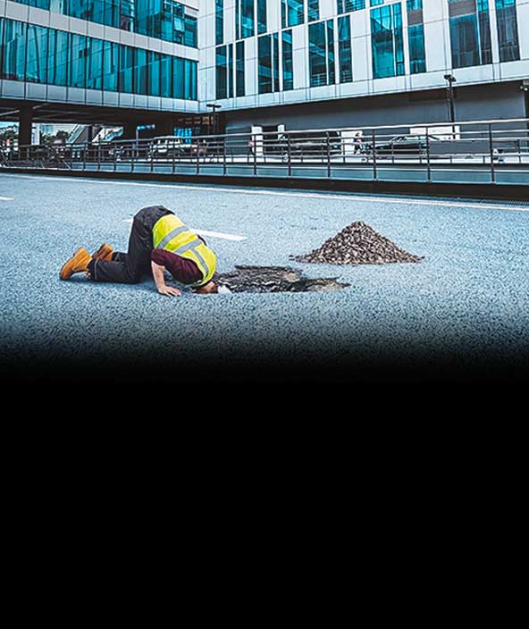 worker placing his head through a hole in the road to look for utilities