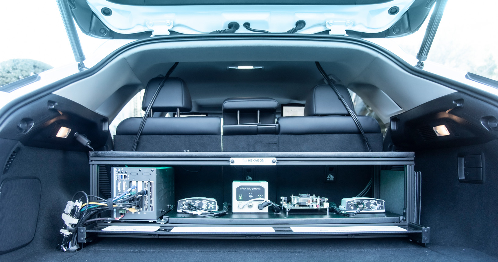 Open trunk of a Lexus car displaying various hardware to enable autonomous operation.