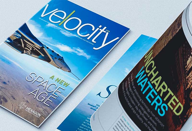 Uma das revistas da Hexagon chamada "Velocity" com a matéria "A New Space Age" sobre uma mesa.